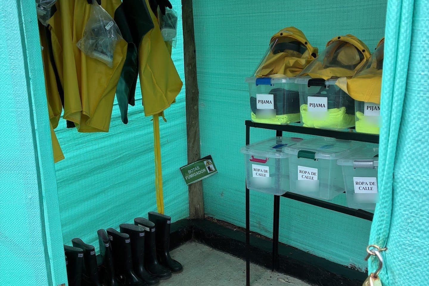 Vestidor de aplicadores con trajes impermeables colgados y cajas rotuladas que separan la ropa de trabajo de la de calle